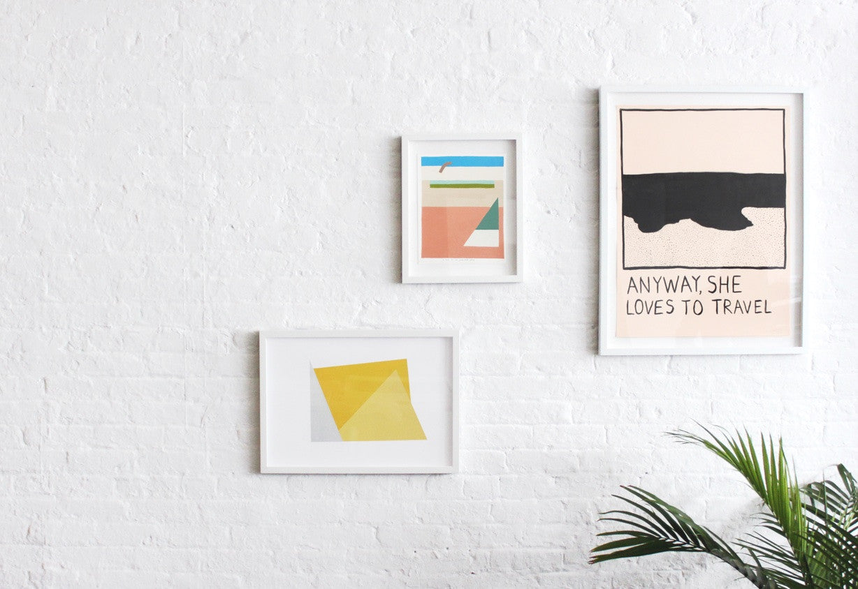 Simply Framed Gallery Frames in White featuring artists courtesy of Uprise Art on a white brick wall with a plant