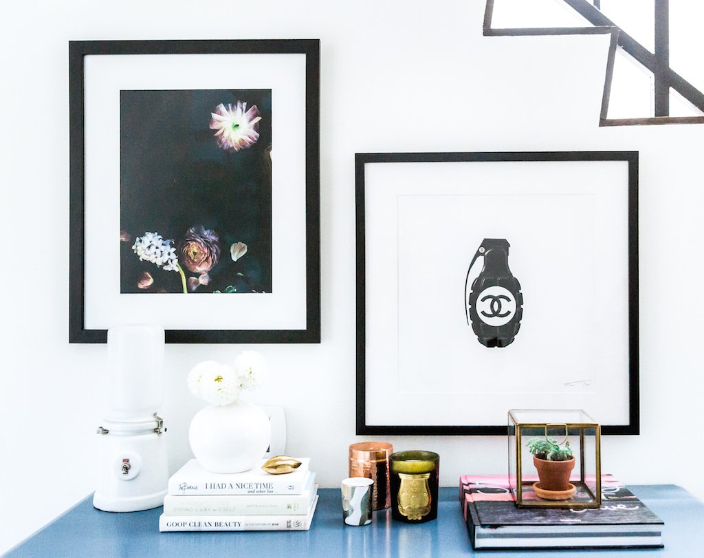 2 art prints framed with a white mat in black against a white wall with a full end table 